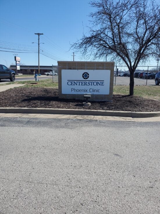 Centerstone Phoenix Clinic sign beside a street, with a tree and parking area behind it.