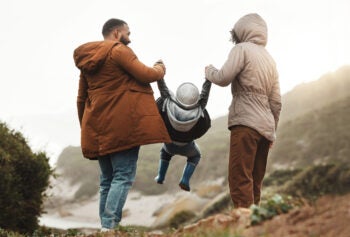 Nature fitness, holding hands and hiking family of mother, father and child walking, play and bond on mountain adventure. Love, freedom peace or back view of winter people trekking on outdoor journey