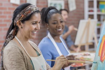 Diverse female friends paint together during art class