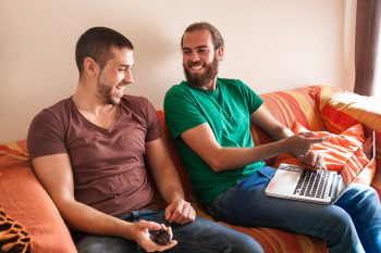 Brothers having fun on a couch with laptop and remote smart tv control