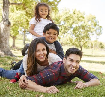 Young kids and parents lying in pile on the grass, portrait