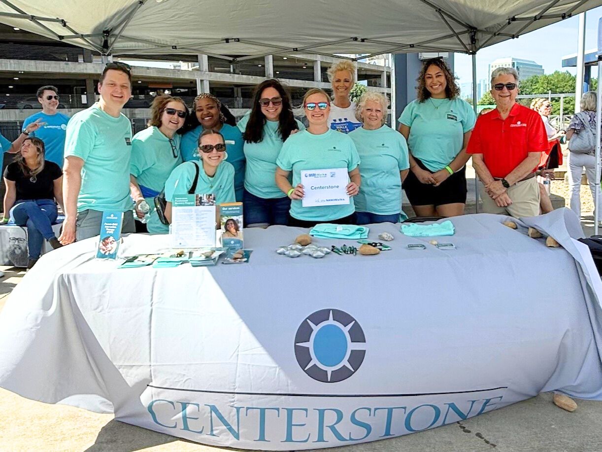 Several Centerstone staff posing and smiling behind a table as they share brochures, cards, and swag at an event.