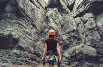 Climber woman standing in front of a stone rock outdoor