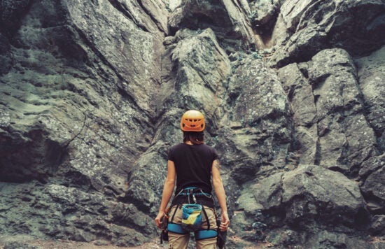 Climber woman standing in front of a stone rock outdoor