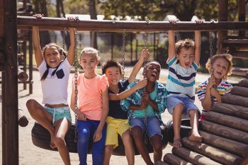Schoolkids having fun on tyre swing at school playground
