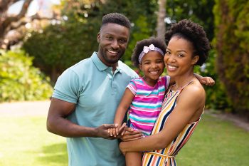 Portrait of smiling african american parents carrying cute daughter standing at garden. family, love and togetherness concept, unaltered.