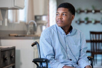 Teenage boy in wheelchair at home gazes out window