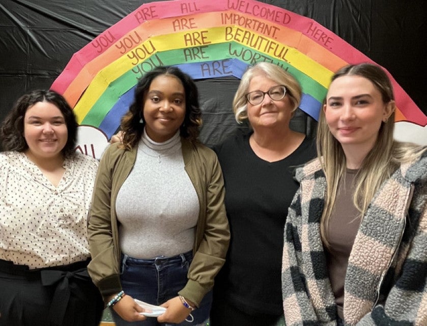 A small group of Centerstone Psychosocial staff posing for a photo in front of a rainbow backdrop with inclusive messaging.