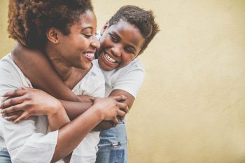 Happy young mother having fun with her child – Son hugging his mum outdoor – Family lifestyle, motherhood, love and tender moments concept – Focus on kid face