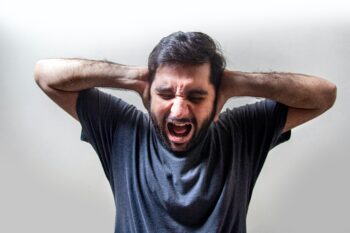 man holding hands over ears screaming