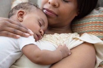 African American mother sleeping on sofa with baby