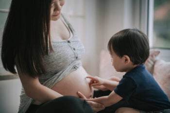 asian chinese baby boy touching his mother’s abdomen express love and anticipation for his little sibling new born