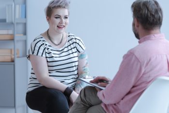 Smiling young woman with tattoos talking with counselor about business