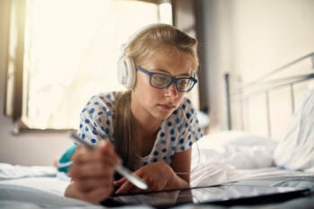 Teenage girl doing homework online using laptop and digital pen